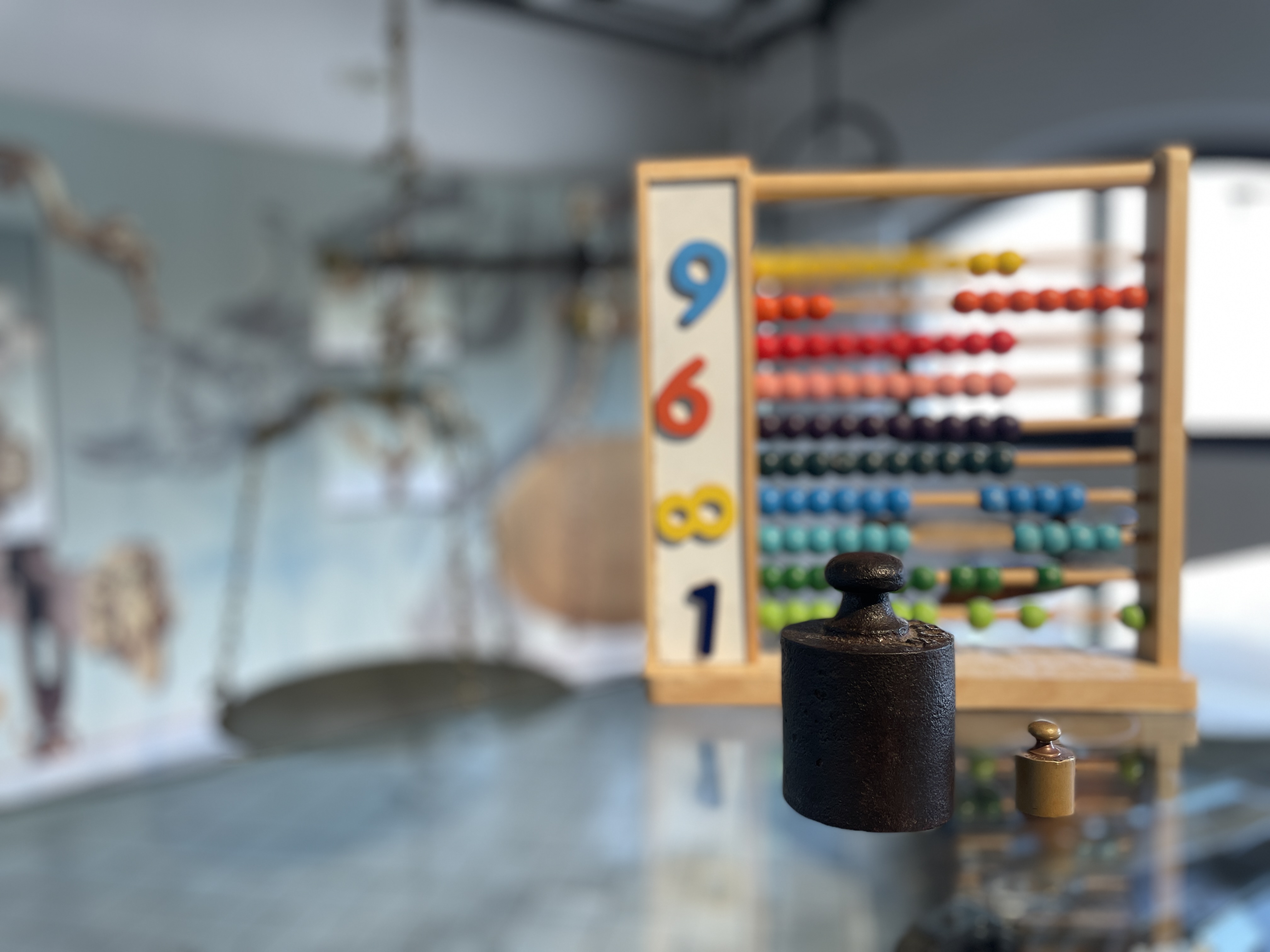 Un pallottoliere con numeri e palline colorate; in primo piano due pesi per bilancia di diversa misura
