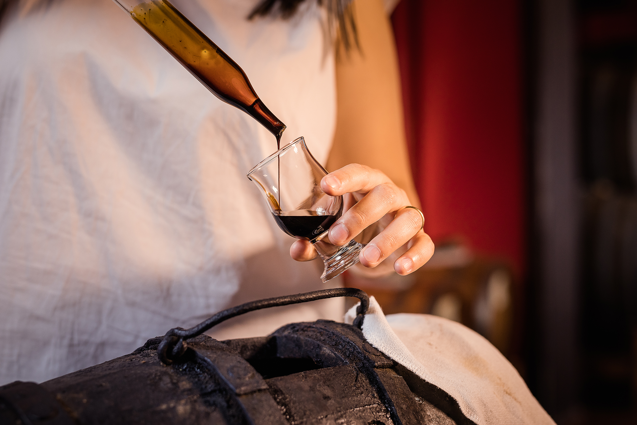 La mano di una donna regge un piccolo calice in cui viene spillato l'aceto balsamico.