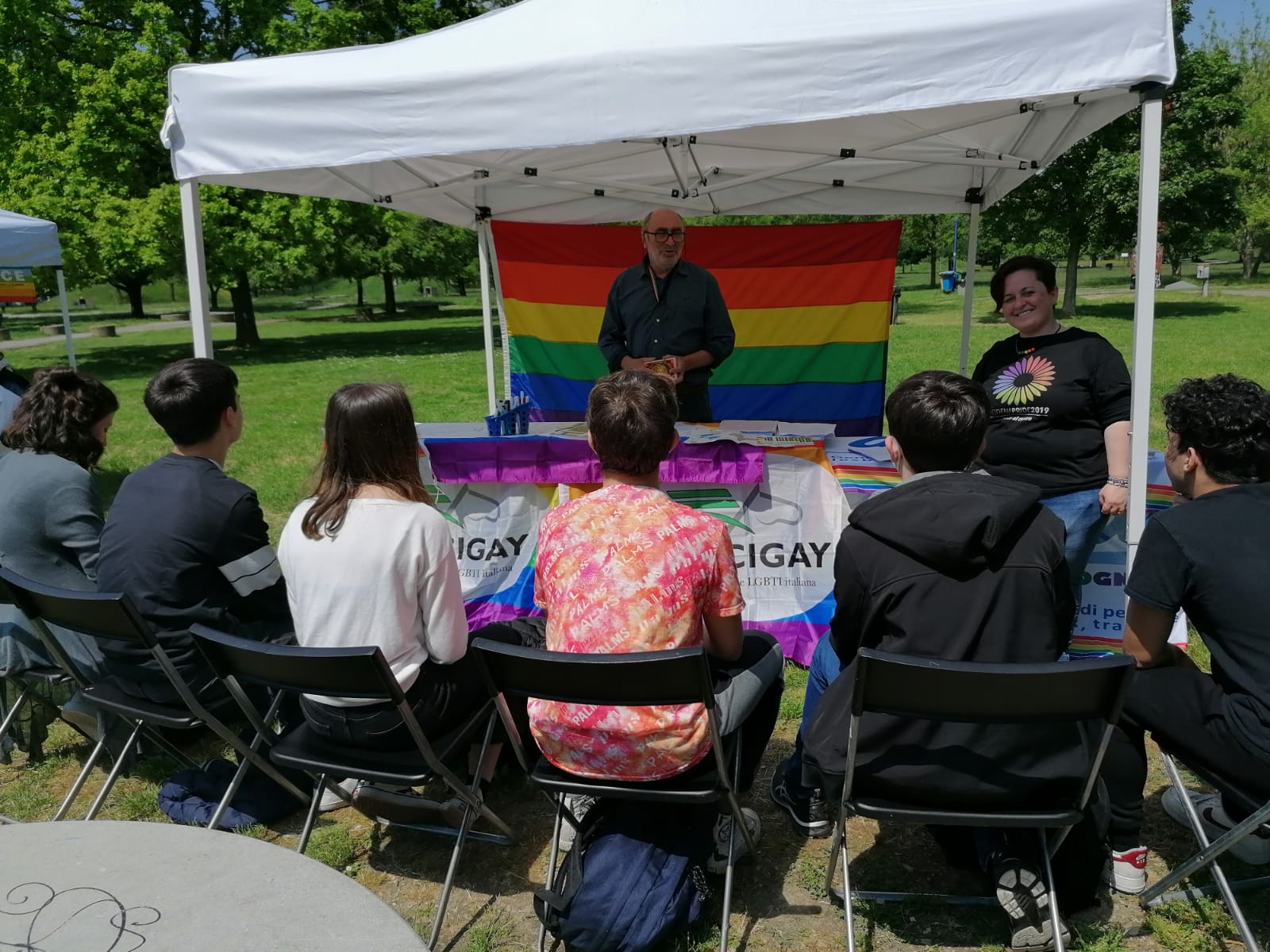 Gazebo con i referenti dell'Arcigay di Modena che presentano il progetto e ragazzi di spalle che ascoltano