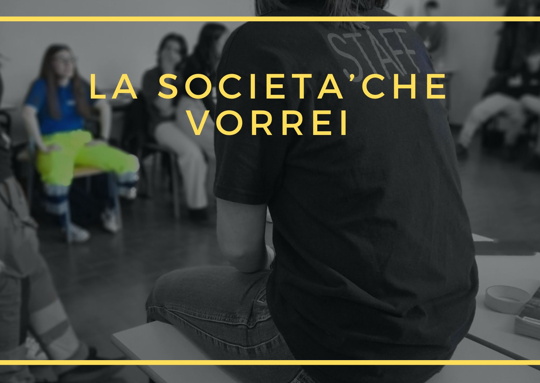 Ragazzi ripresi di spalle mentre il relatore parla e la scritta "La società che vorrei" in giallo sopra l'immagine.