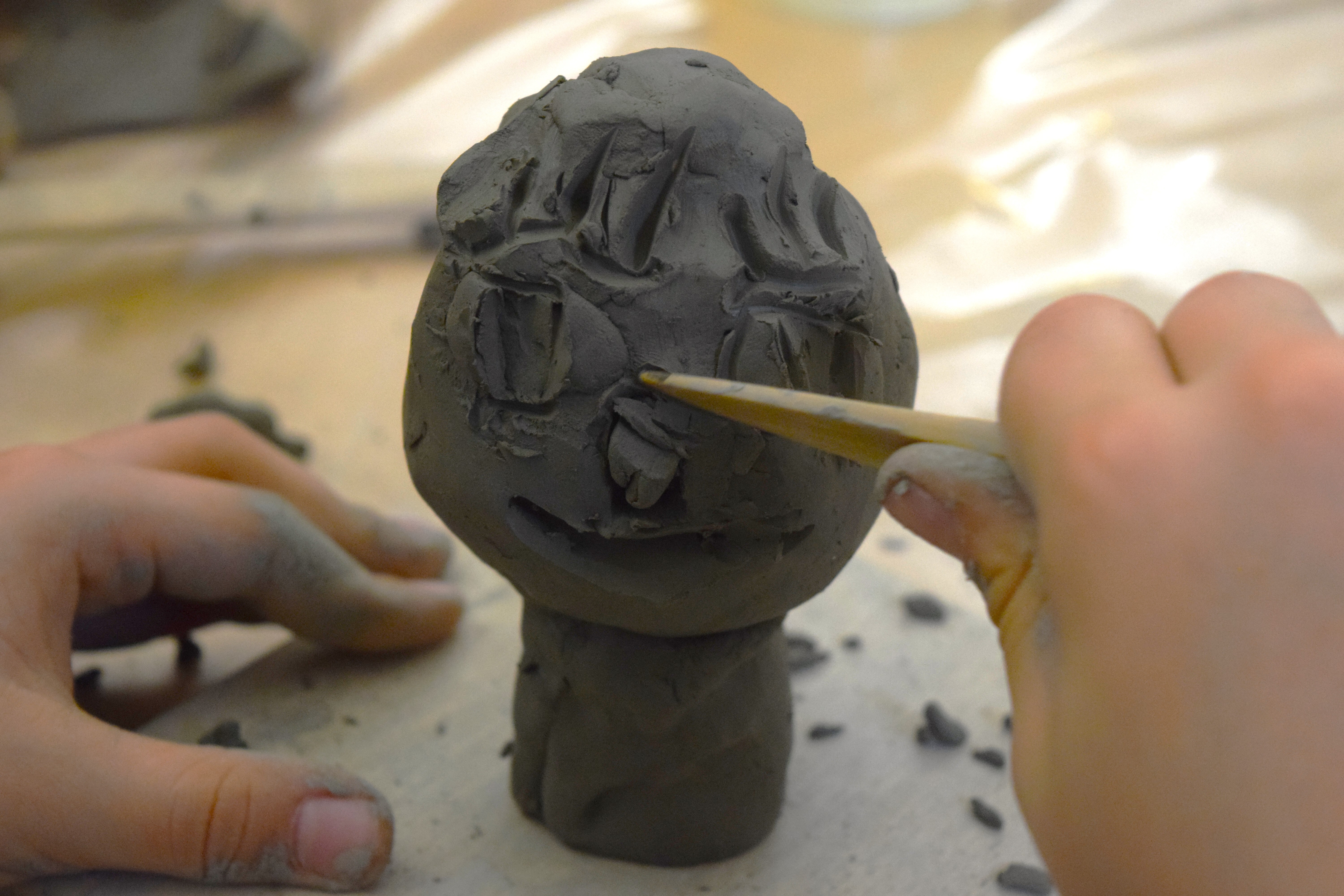 Una bambino che definisce i tratti di un volto di una scultura in argilla con un bastoncino di legno 