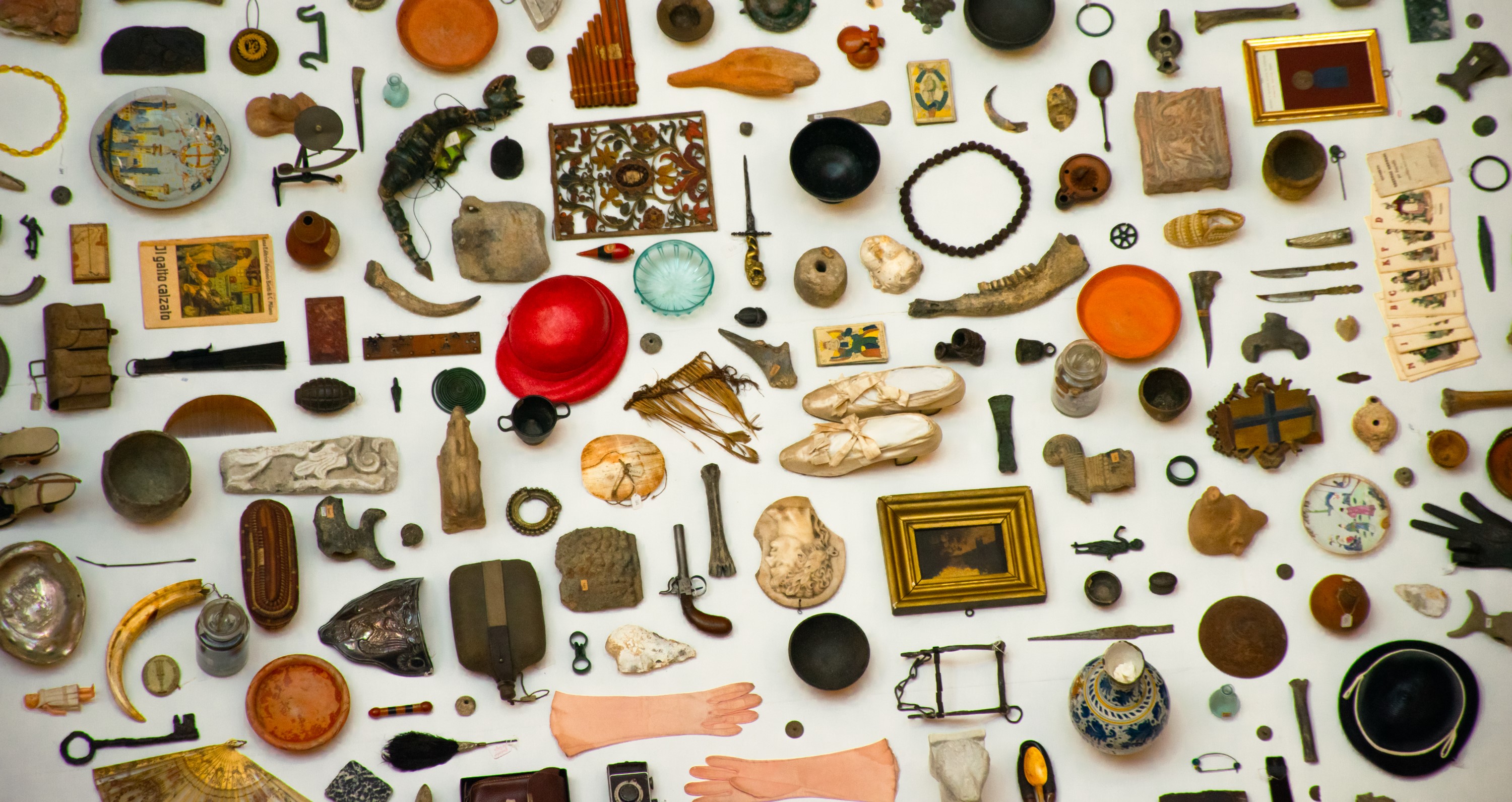 Raccolta di oggetti diversi disposti su fondo bianco: reperti, strumenti, frammenti e opere.