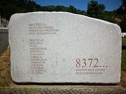 Una grande stele in pietra, con un elenco di nomi inciso sul lato sinistro e il numero 8372 sulla destra, accompagnato dalla scritta che significa "numero finale delle vittime accertate".
