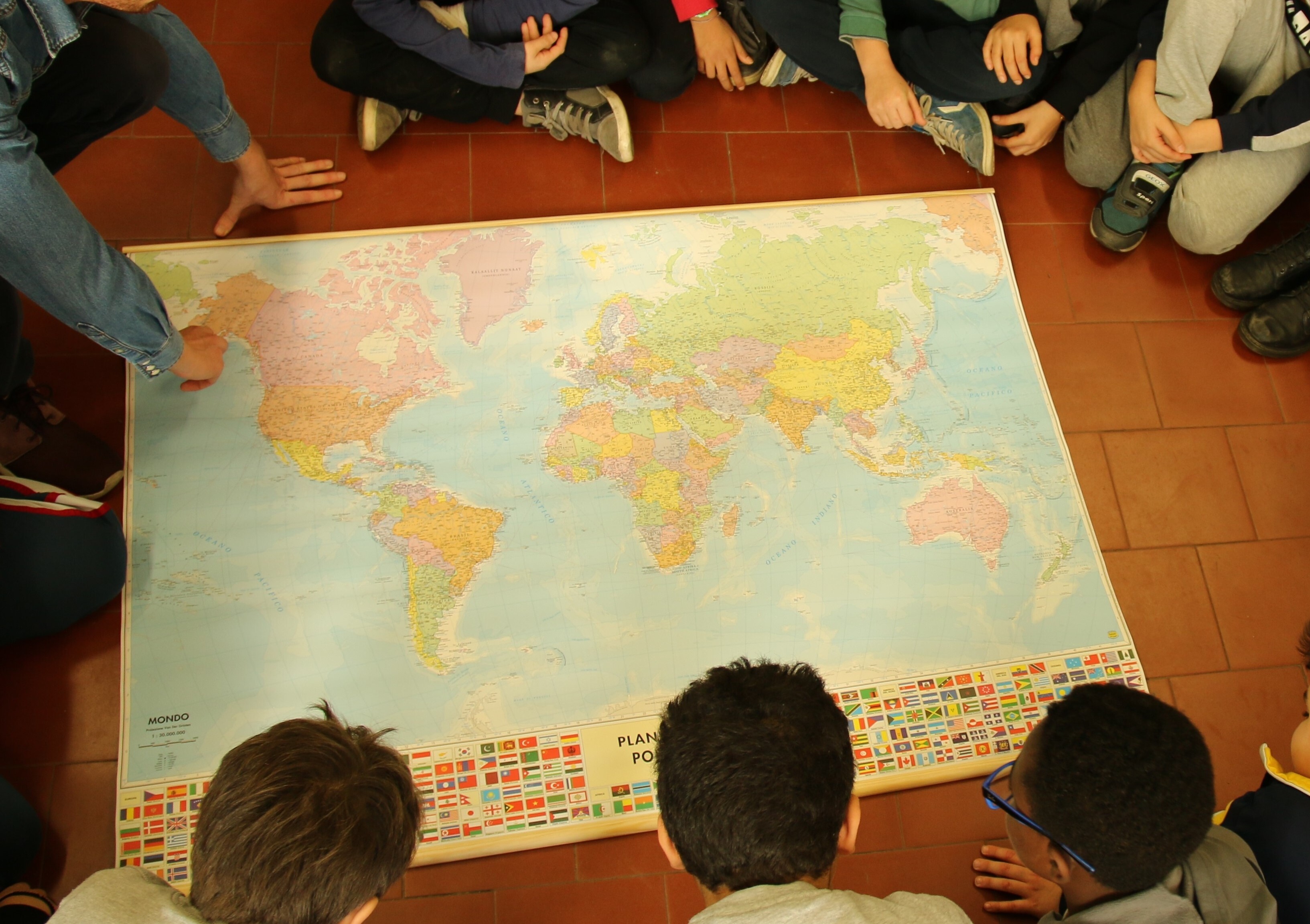 Bambini che guardano una mappa del Mondo appoggiata a terra.