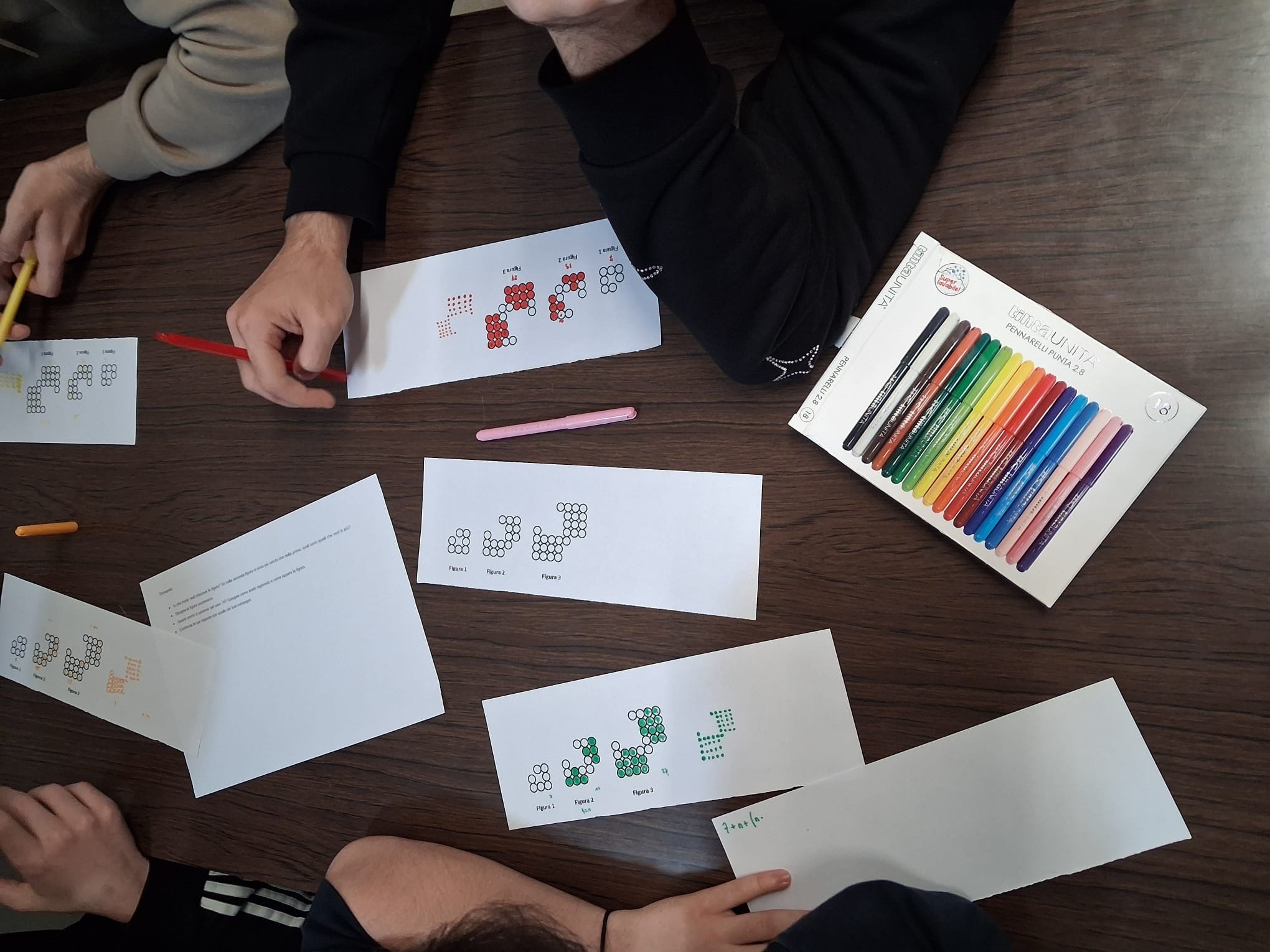 Studenti che provano a risolvere in gruppo la sfida matematica "Circle Fever" seduti sul pavimento della biblioteca Delfini.